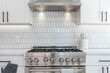 Modern kitchen details of white granite counter, gas stove, and white tile backsplash.