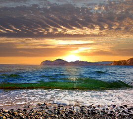 Wall Mural - Sunset over the Black Sea coast, Crimea, Picturesque sunset view over the Black Sea coast, near Koktebel. The Karadag mountain range is visible in the distance. Waves roll on the rocky shore