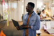 © Drazen - Happy black entrepreneur uses laptop while examining mind map on glass wall at casual office.