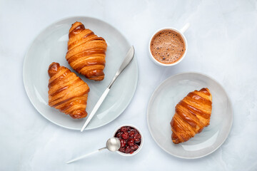 Croissants with jam and coffee. Two gray plates on a marble table. Top view, flat lay. A cup of hot chocolate in the morning for breakfast. French culture. Food background.