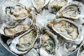 many kinds opened oysters in a plate with ice and lemon on blue background, Healthy food, gourmet food. Oyster dinner in restaurant. top view