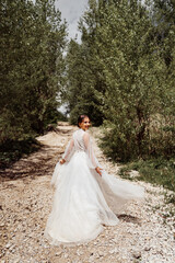  view from back. bride in wedding dress walks along mountain path between trees.