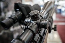 Black shooting scope optics mounted on rifle displayed at weapons exhibition fair, closeup detail to adjustment knobs