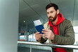 © NFstock - Horizontal photo of confident, good-wearing man indoor airport terminal or railway station. He holding passport in hands and looking at the ticket with pleasure smile