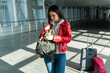 © NFstock - Calm concentrated woman putting something at her backpack while standing at the airport hall near her luggage. Stock photo