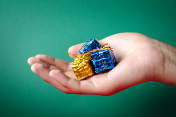 hand of a man holding Christmas presents, giving gifts in front of green background.