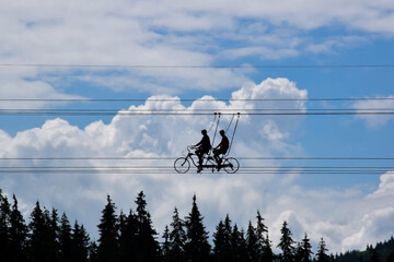 Two people of unrecognizable appearance ride high in the sky on special bicycles on the ropes at the attraction