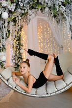 A Girl In A Gym Suit Stretches On A Round Swing With Christmas Decorations In The Interior, Decorated For The New Year. The Concept Of Christmas Holidays.