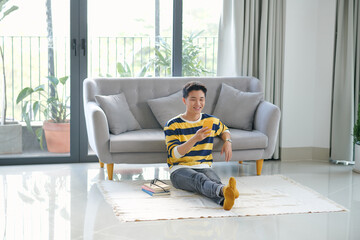 Wall Mural - Young male sitting on the floor in the living room and having video call via phone