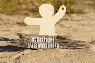 On the sand near the wooden figurine of a man there is a piece of wood with the inscription - Global Warming