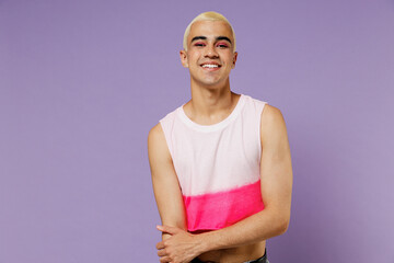 Young blond cool fun latin gay man 20s with make up wearing fashionable bright pink top look camera isolated on plain pastel purple background studio portrait. People lifestyle fashion lgbtq concept.