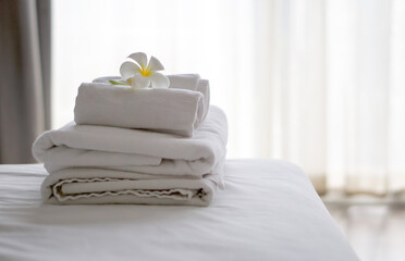 Two white towels with white flower on clean bed in hotel room with blurred background. Summer holiday and vacation concept.