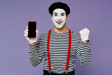 Young Mime Man With White Face Mask Wear Striped Shirt Beret Hold Mobile Cell Phone With Blank Screen Workspace Area Do Winner Gesture Isolated On Plain Pastel Light Violet Background Studio Portrait
