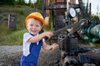 © anatoliy_gleb - Adorable little boy in construction helmet using industrial wrench while repairing pump jack pipe. Cute kid in work overalls looking aside and smiling while tightening bolt on pipe.