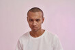 © Svitlana - Portrait of focused young mixed race man in casual white t shirt looking at camera, standing isolated over pink background