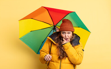 Wall Mural - hispanic pretty woman with mouth and eyes wide open and hand on chin. umbrella concept