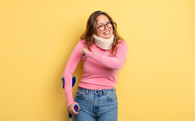 Wall Mural - hispanic pretty woman feeling happy and facing a challenge or celebrating. crutch and collar accident