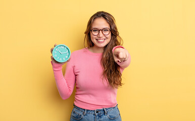 Wall Mural - hispanic pretty woman pointing at camera choosing you. alarm clock concept