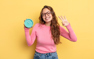 Wall Mural - hispanic pretty woman smiling and looking friendly, showing number three. alarm clock concept