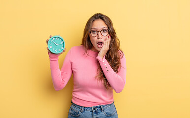 Wall Mural - hispanic pretty woman feeling shocked and scared. alarm clock concept