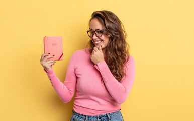 Wall Mural - hispanic pretty woman smiling with a happy, confident expression with hand on chin. agenda concept