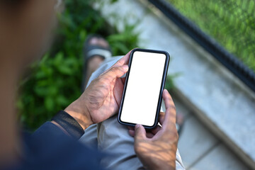 Poster - Top view image of a man's hand holding a white blank screen smartphone while sitting next to the wire mesh fence.