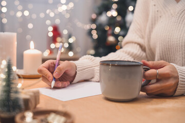 Goals plans make to do and wish list for new year christmas concept writing in notebook. Woman hand holding pen on notepad and coffee cup at home on winter holidays xmas.