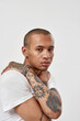 © Svitlana - Portrait of serious young mixed race tattooed guy in white t shirt posing for camera isolated over white background