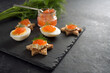 Red caviar on halved eggs and on toasted canapes in star shape with dill, preparation for a festive Christmas buffet on a dark slate plate, large copy space