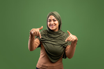 Look there. Positive arab lady pointing down with two fingers, demonstrating free place for your design or advertisement