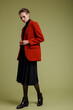 © SBekhinov - Fashion photo of a beautiful elegant young woman in a pretty suit, red jacket, black transparent blouse, short pants posing over green background. Studio Shot. Full length portrait