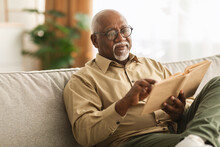 Senior African Man Reading Book Sitting On Couch At Home