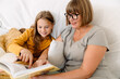 © Drobot Dean - White girl reading book with her grandmother while sitting on sofa