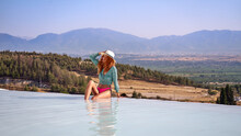 Pamukkale Travertine In Turkey With Woman Enjoying The Views. Red Hair Woman Traveler Swimming At Pamukkale Natural Park And Looking At Beautiful Sunset.Sexy Young Woman Rest In Pamukkale.           