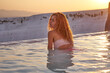 © Hryhorii - Young woman enjoying the views of Pamukkale travertine in Turkey. Red hair woman traveler swimming at Pamukkale Natural Park and looking at beautiful sunset.Sexy young woman rest in Pamukkale.