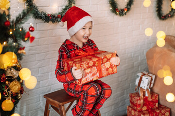 Canvas Print - Boy in pajamas and santa hat on his head holding big gift