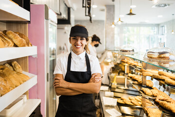 beautiful young and happy female worker working in a modern bakery. she is posing and looking at cam