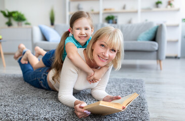 Wall Mural - Happy mature woman and granddaughter reading book at home