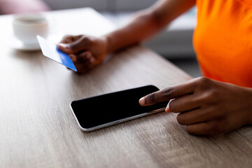 Unrecognizable black woman using smartphone and credit card for online shopping on table, mockup for app or website