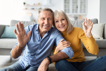 Wall Mural - Cheerful Older Couple Waving Hands To Camera Sitting At Home