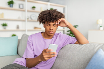 Canvas Print - Funky black teen guy with mobile phone studying online, messaging with friend, posting in social network from home