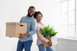 Smiling young african american husband and wife holding cardboard boxes with plant in pot