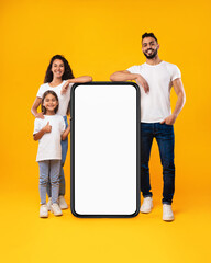 Wall Mural - Middle-Eastern Family Standing Near Big Blank Phone Screen, Yellow Background