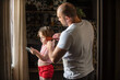 © Ольга Рязанцева - The father takes part in the upbringing and care of his children. A man is combing his little daughter's hair with a comb, a girl is looking at the phone, at home.