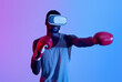 Young black guy in VR headset wearing boxing gloves, making punch in neon light. Exercising with virtual reality concept