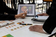 © kamiphotos - Two people look at the tablet screen showing the company financial summary, business people brainstorm ideas to solve losses and plan strategies to make the company profitable and grow.