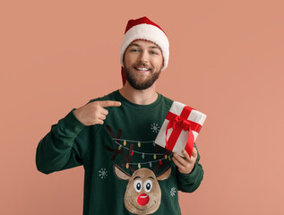 Canvas Print - Young man in Santa Claus hat and with Christmas gift on color background