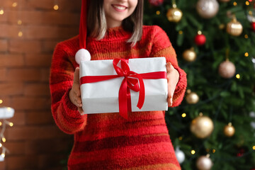 Beautiful young woman with gift at home on Christmas eve