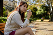 © photok - コーヒーカップを持ってベンチに座っているアジア人女性