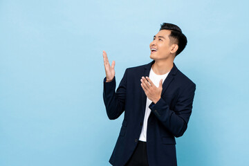 Young smiling Asian man opening hands and looking up sideways in isolated light blue color background